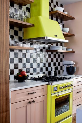 A maximalist designed kitchen worktop with neon yellow cabinet and oven. There are peach-colored cabinets and a black-and-white checkerboard backsplash.