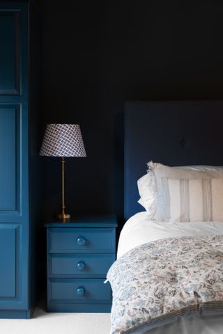 Hague blue bedroom where bedside table, wardrobe and headboard are all painted in the shade. The bed is furnished with white and beige linens.