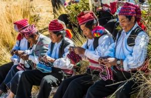 A group of Peruvian artisans in traditional clothing weave colorful textiles in a rural community.