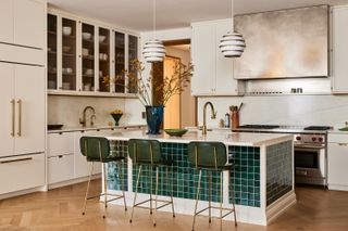 A view of a kitchen island with dark green tiles and three green stools