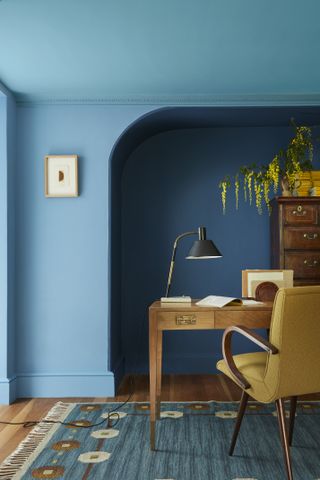 Blue drenched home office with yellow chair and furniture