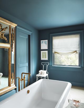 Corner of a bathroom decorated in blue colors with a white bathtub and an ornate gold mirror in view