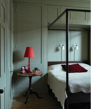 Bedroom with colorful gray-green walls, a four-poster bed and a bright red lamp on a side table