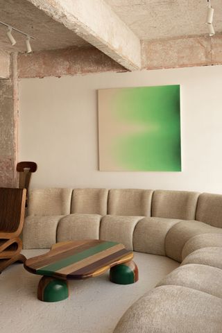 Large curved sofa in an all beige living room with a bright green abstract painting hanging on the back wall above the sofa