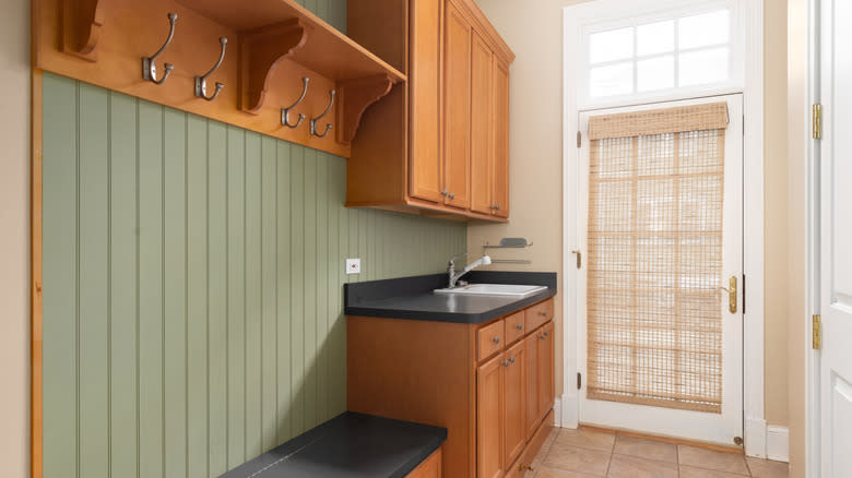 A green entrance area with a bench, sink and wooden cabinets