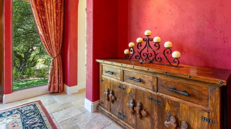 Rust-red entrance area with ornate carpet and antique sideboard