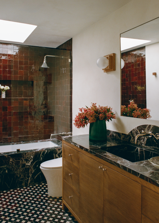 Burgundy tiles surrounding a bathtub with black marble sides and black and white tile floor