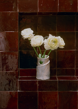 A small white flower vase in a corner decorated with burgundy tiles