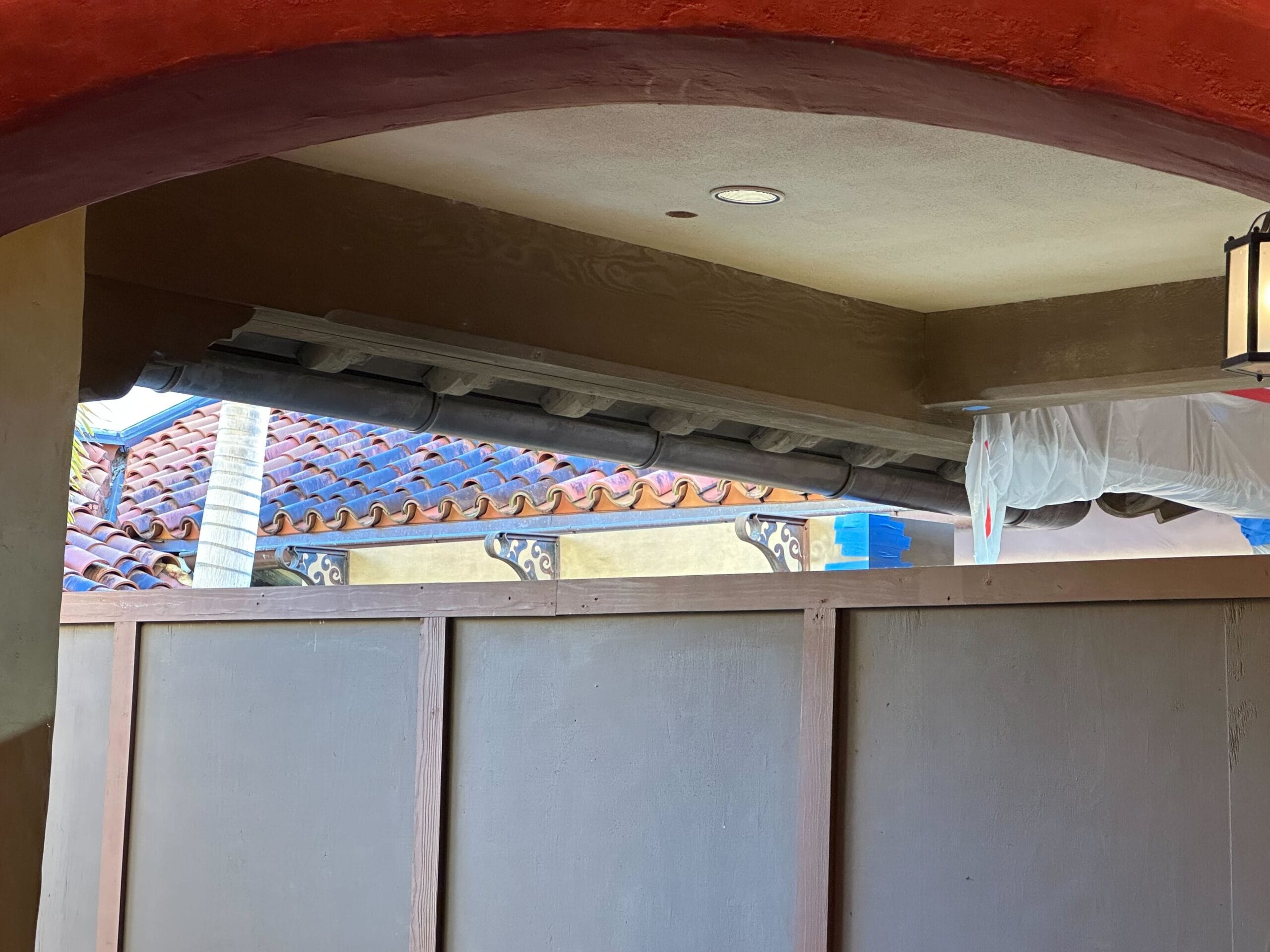 Construction area with partially covered roof and wooden barrier, visible roof tiles and ceiling light.