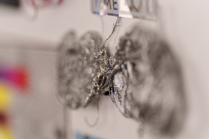 Close-up of tangled metal chains or wires hanging on a wall. The background is blurred with soft colors and patterns, suggesting other objects or decorations nearby.