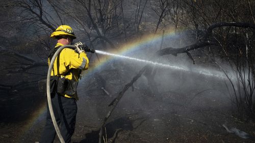 A firefighter uses hoses to extinguish hot spots from the Archer Fire in the Granada Hills neighborhood of Los Angeles.