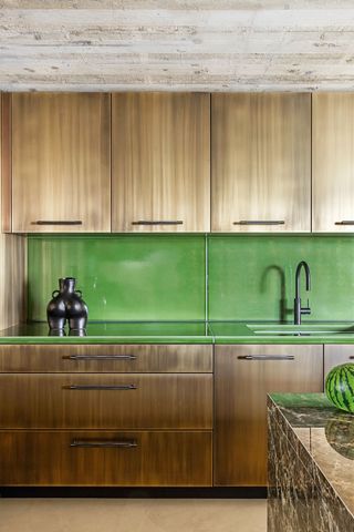 Image of a kitchen countertop and cabinets. The ceiling is concrete and the cabinets are aged brass. The countertops and backsplash are made from a lime green Prolave ​​lava stone material.