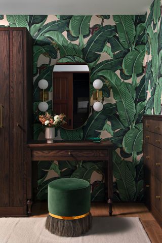 A corner in a bedroom with a green stool and wallpaper and a dark brown wooden cabinet