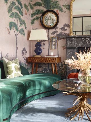 A living room with an emerald green sofa and pink walls