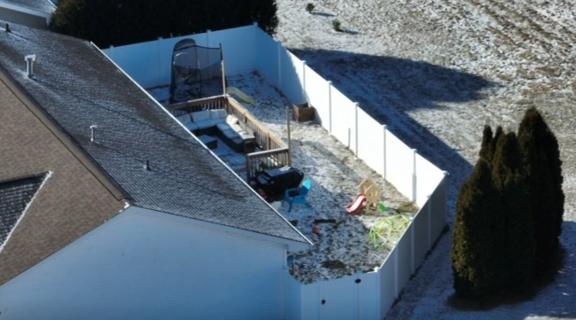 Aerial view of a backyard with a fence, patio and children's play equipment.