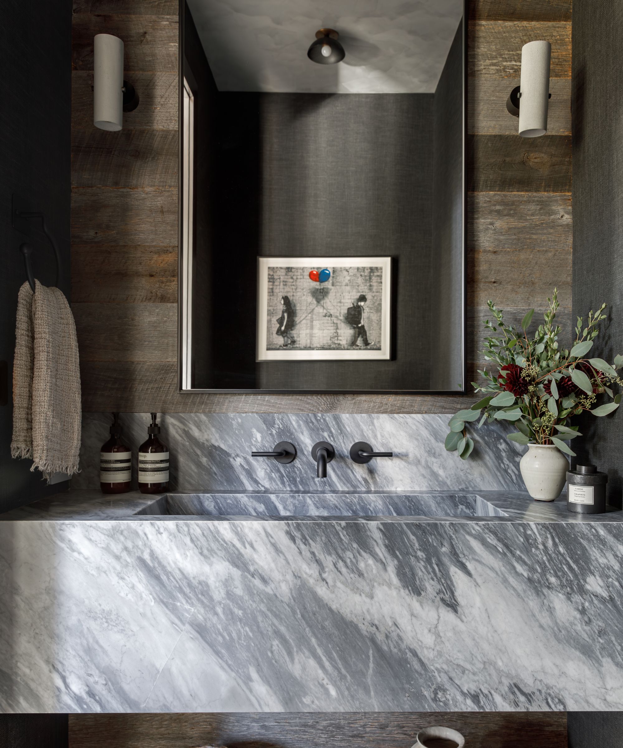 A dark bathroom with a striking stone sink and wooden wall paneling