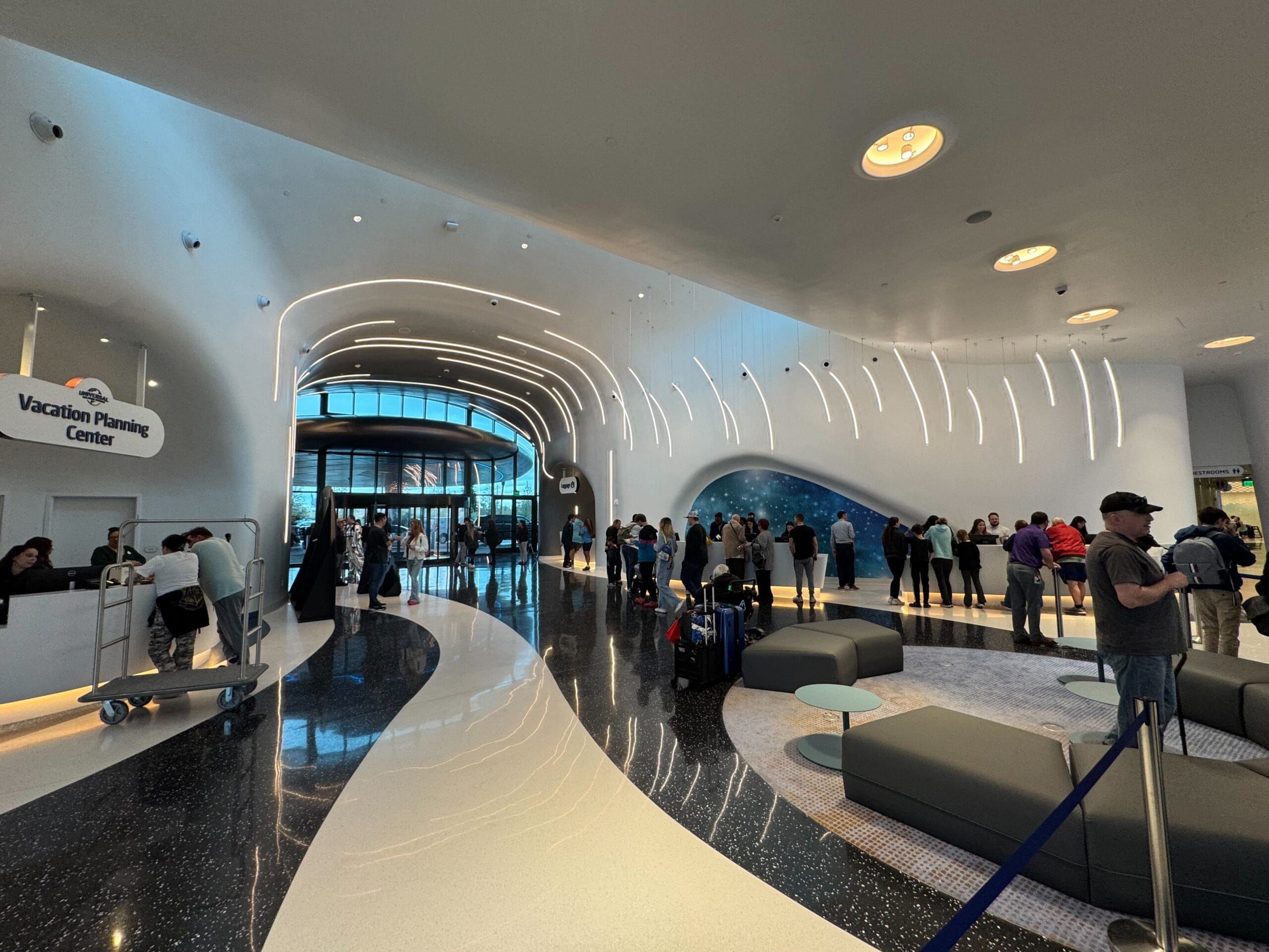 Modern airport lobby with curved architecture, shiny floors and illuminated ceiling. People check in at the counters and form queues. Sign reads "Vacation Planning Center.