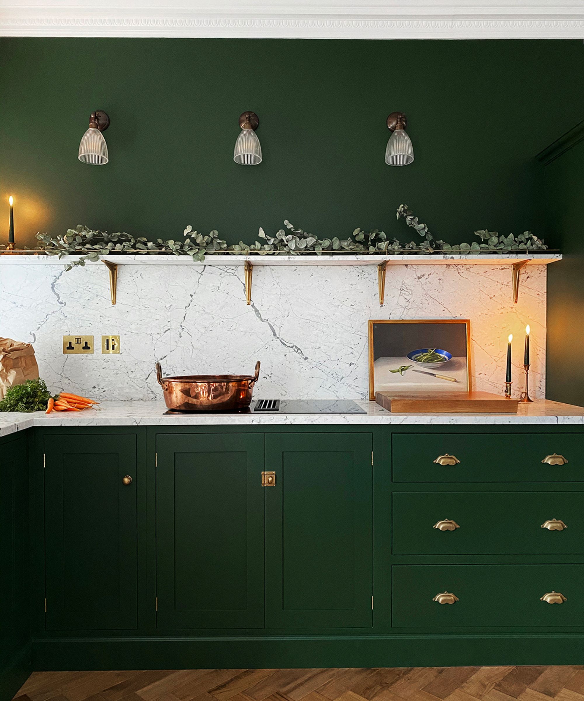 Green kitchen cabinets, parquet floors, white stone counters with glass oven, copper pot, open shelves, green walls and wooden cutting board