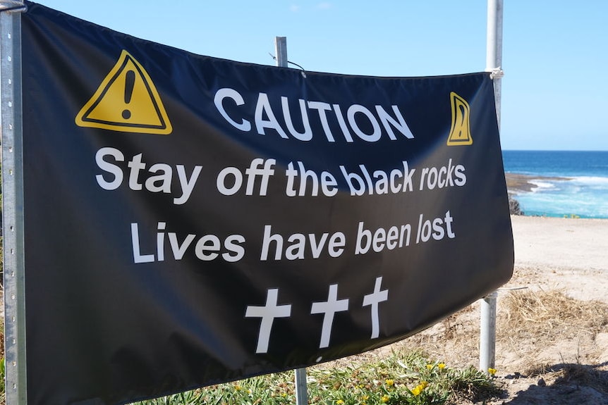 Black sign on a beach warning spectators to keep away.