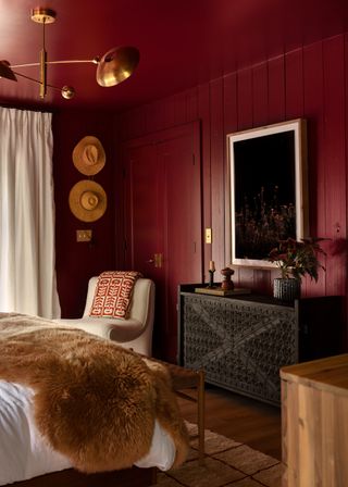 Bedroom in deep red color with fur throw, brass pendant lamp and artwork