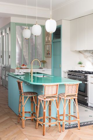 White kitchen with a teal kitchen island and a lava stone countertop. There are rattan bar stools all over the island