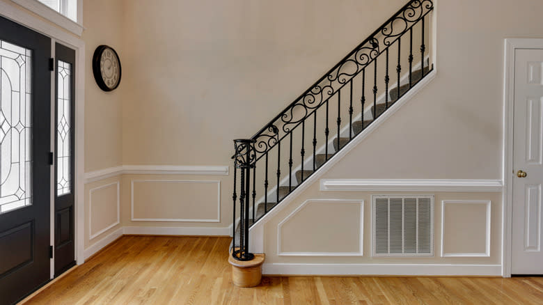 A large, empty, cream-colored entrance hall with a grand staircase and a black door