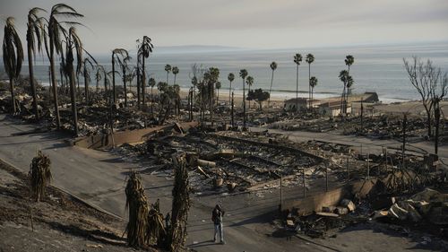 A person walks past damage caused by the Palisades Fire in the Pacific Palisades neighborhood of Los Angeles on Friday, Jan. 10, 2025. (AP Photo/John Locher)