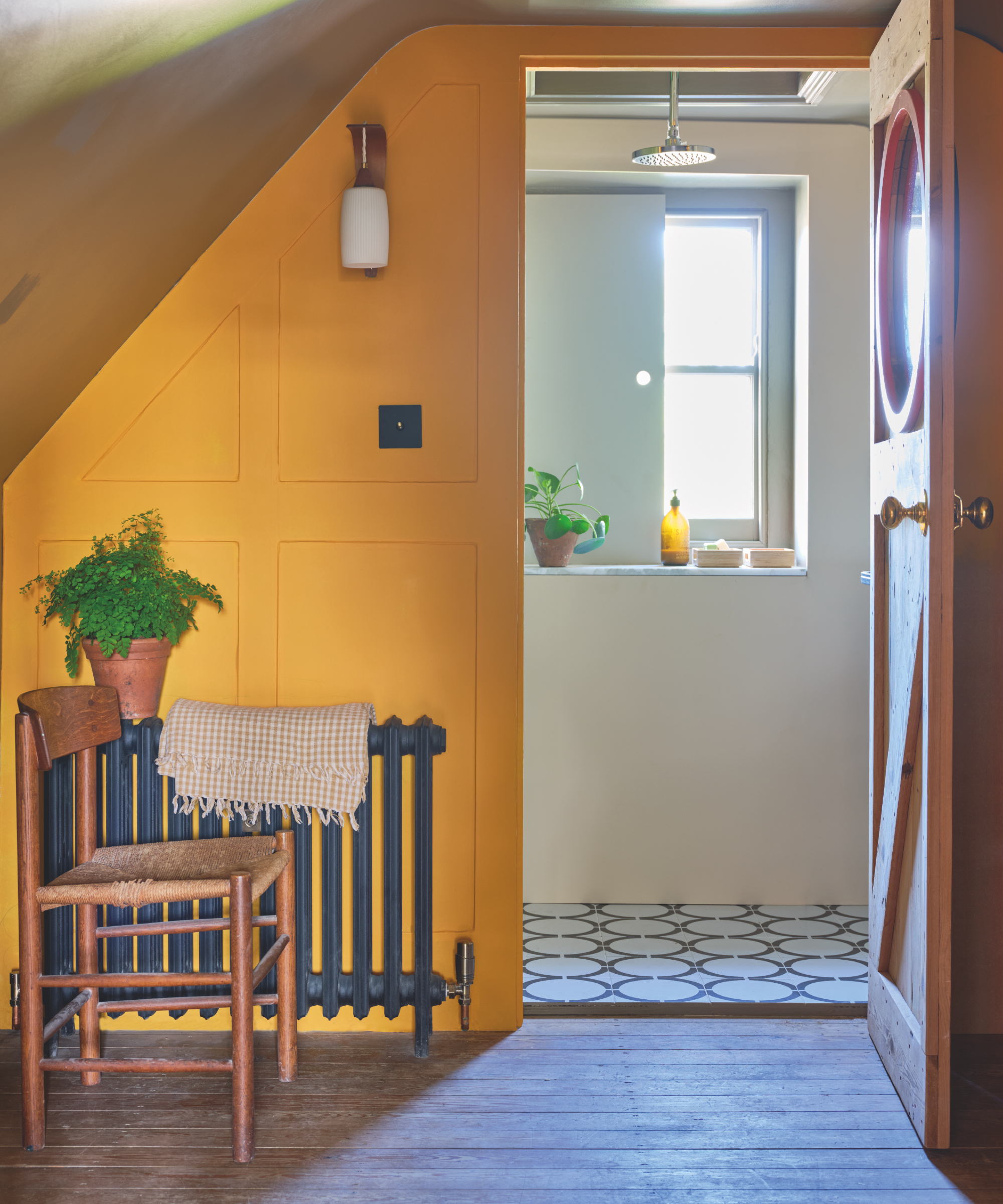 Landing with wooden planks, chair, charcoal gray cooler, yellow painted cladding, view of the bathroom, circular blue tiles, windows, windows