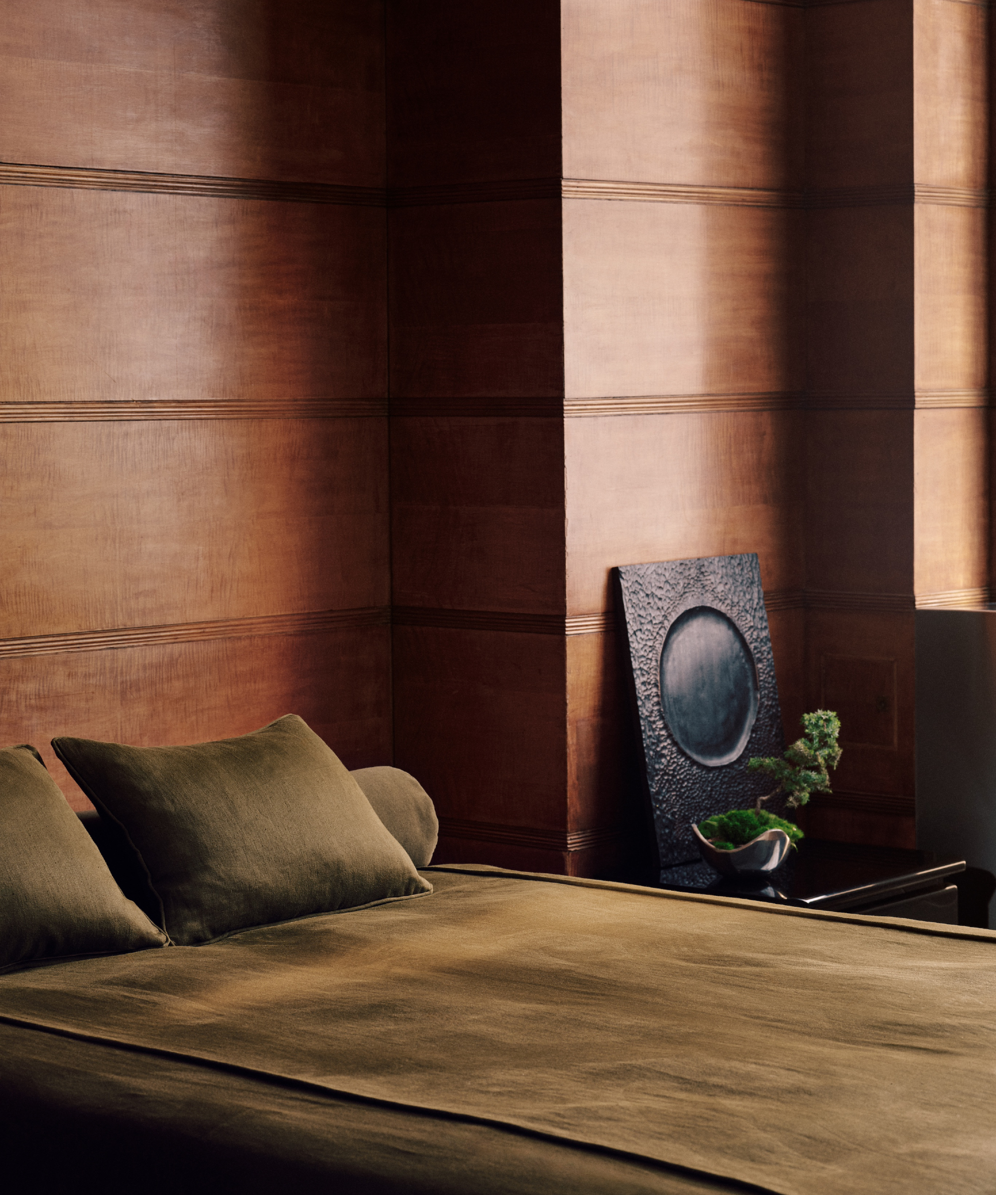 Bedroom with wood paneling and rich olive bed linen, side table, black mirror