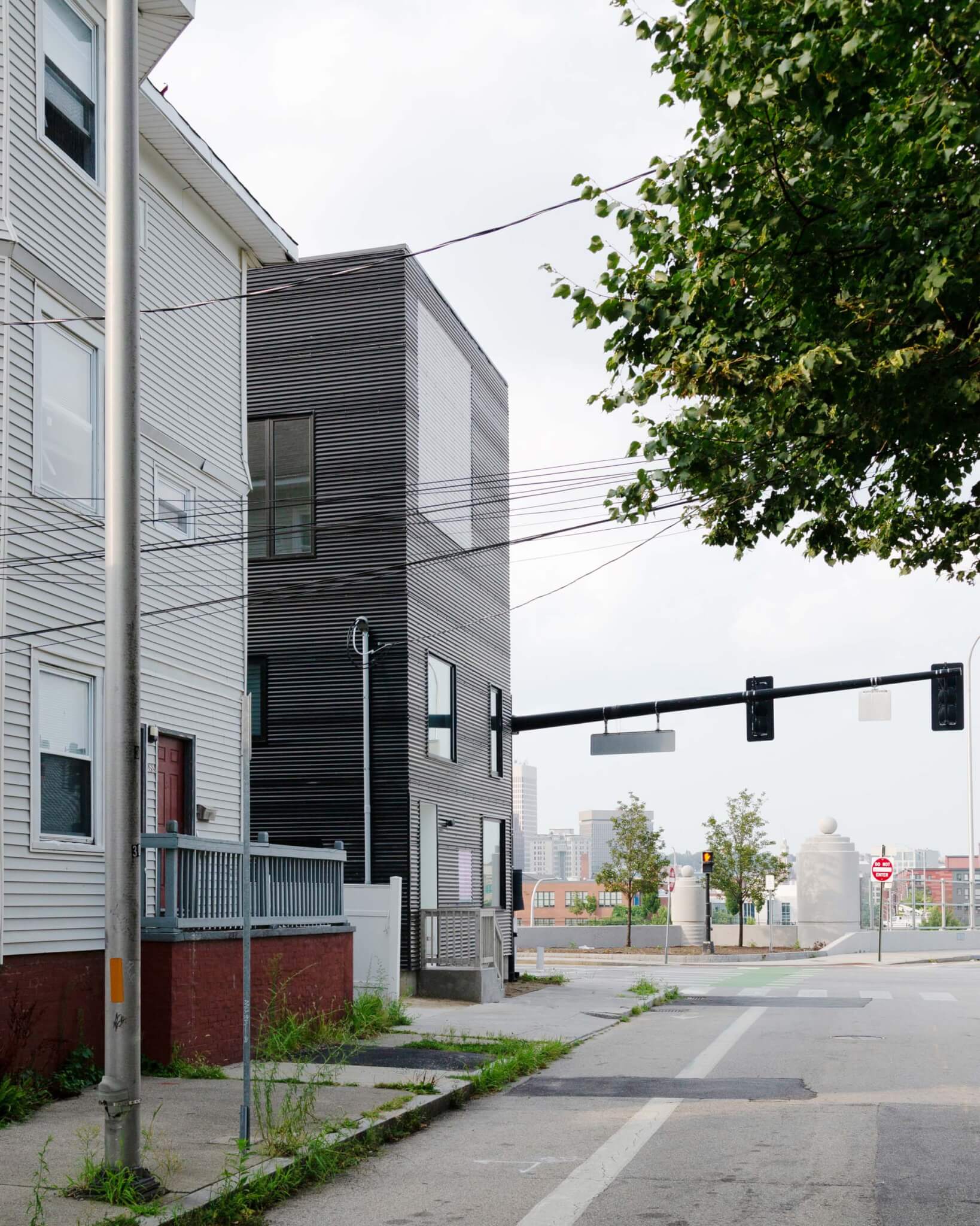 The house is covered with black corrugated iron metal along a street with residential buildings in size