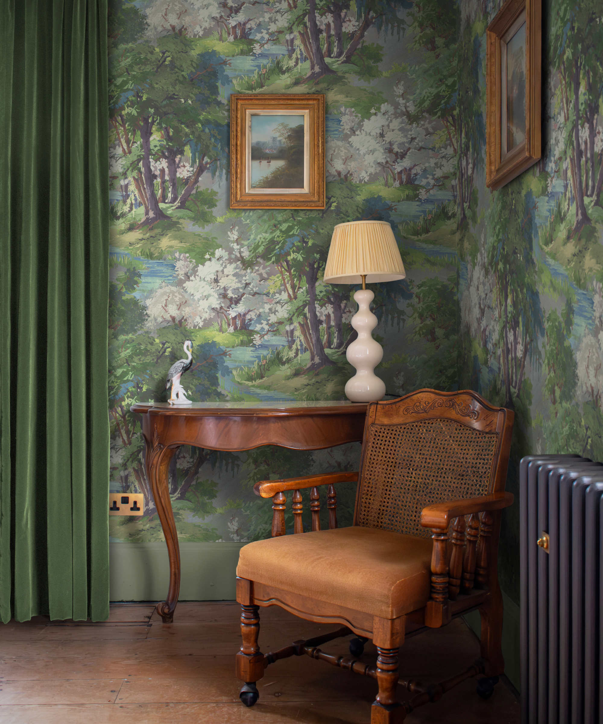 Corner in the living room with forest/wood -style wall presentations for green velvet, mahogany armchair and console, lamp, works of art, cooler