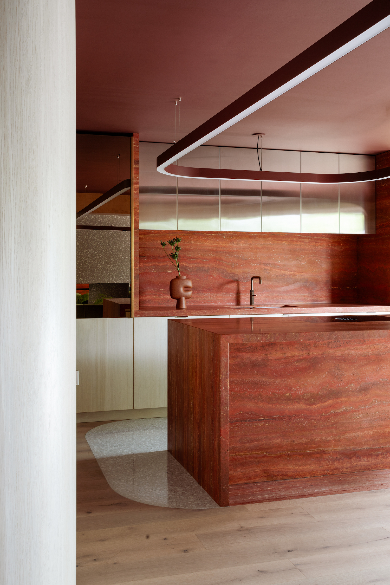 A red/orange marble counter and a backpar with blonde wooden floors