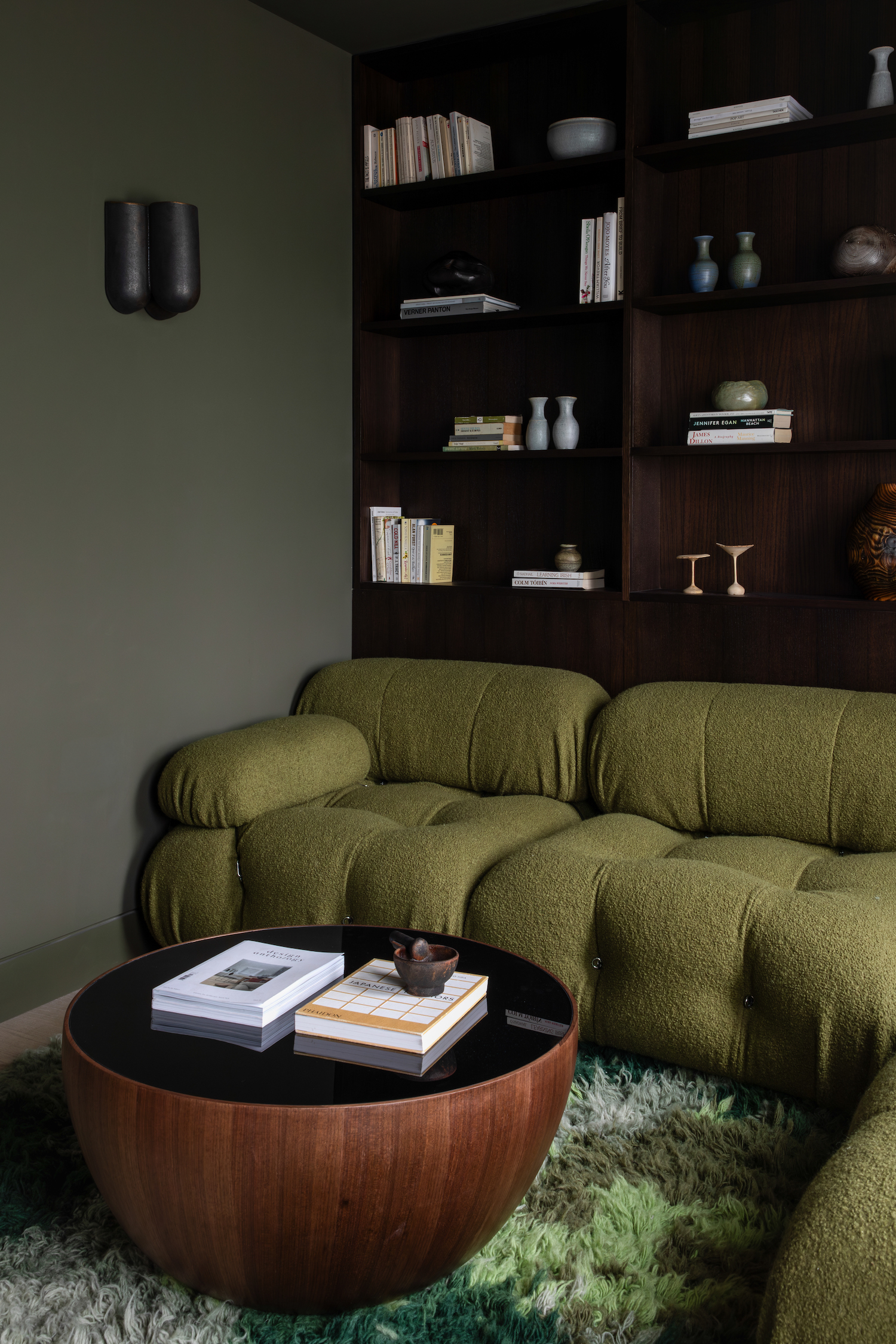 A sage green living room with green sofa, dark wooden book shelf and circular coffee table