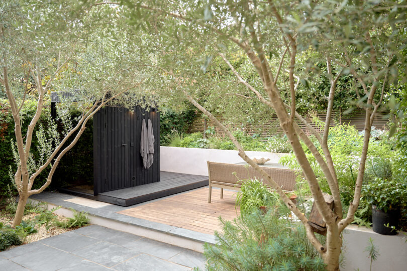 Garden with trees and plants, a wooden deck, outdoor furniture and a black outdoor sauna