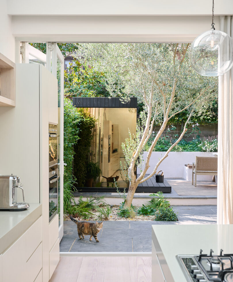 Heller kitchen area with large windows and open doors that lead to a lush garden with trees and plants. Neutral -colored curtains and furniture contribute to the airy ambience