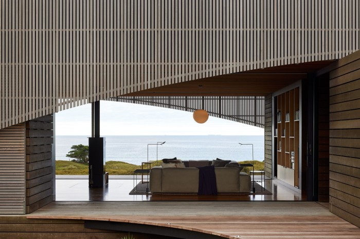 Silvered wooden slats with a curve cut into it reveal space behind the glass and sea view through the other side