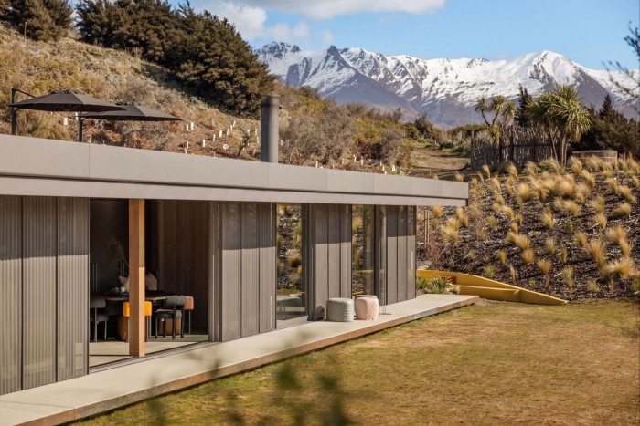 Low gray metal, wood and concrete house with snow -covered mountains in the distance