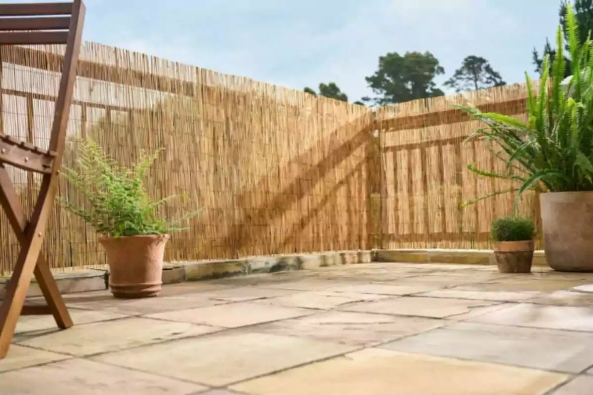 A terrace decorated with a tiled floor, with potted plants and a bamboo fence next to a wooden chair.