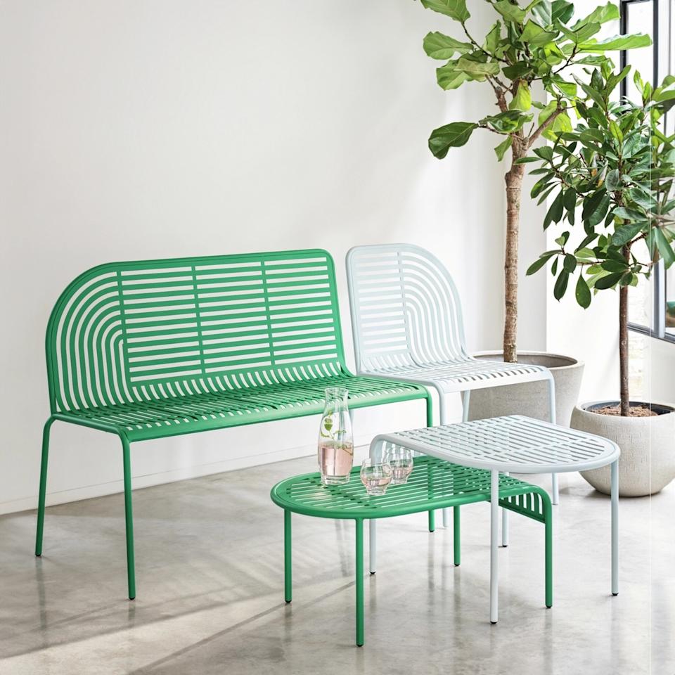 Image of a green -green and light blue garden bench and suitable nesting table. They are staged in a room with white walls, concrete floors and two pot trees.