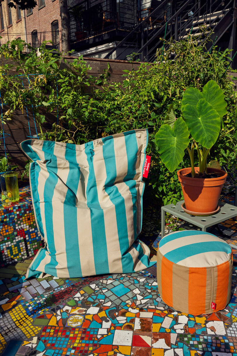 Strip blue and beige beanbag next to a plant on a small table in a colorful tiled area outdoors