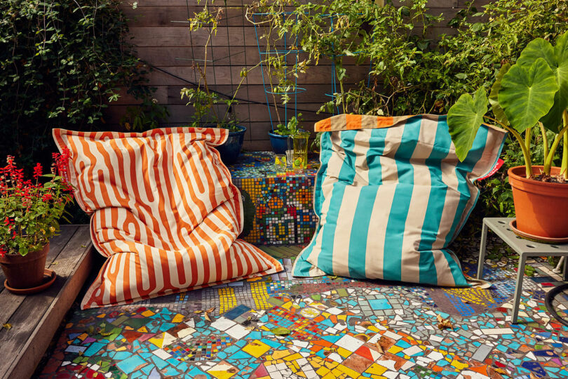 Two large patrol bean bags, one orange and white, the other blue and white, sit on a colorful mosaic terrace that is surrounded by plants and a wooden fence