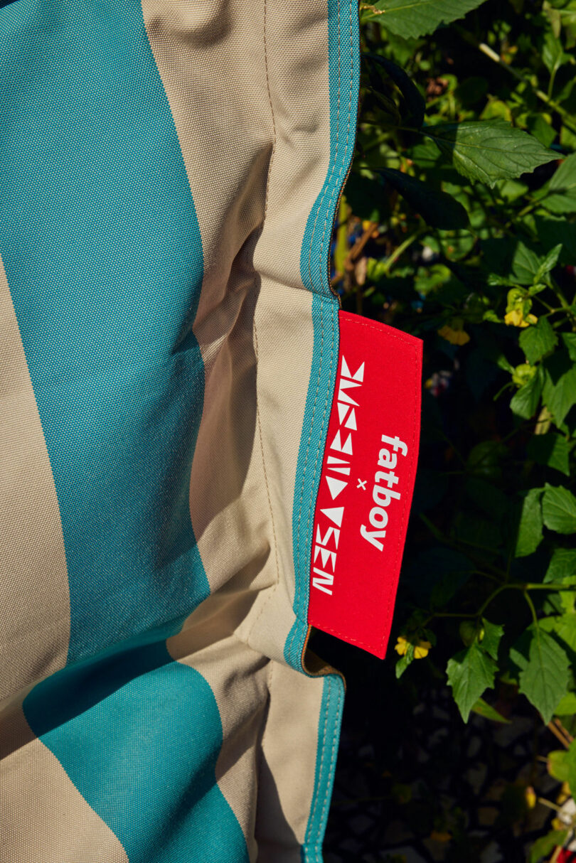 Close up of a turquoise and beige striped fabric "Fatboy" and outdoor plants in the background