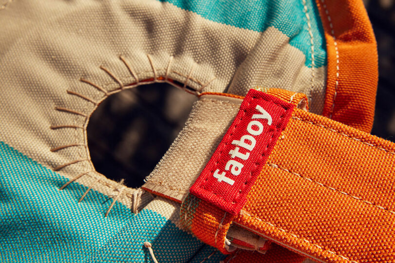 Closure of a detergent Ös with frayed edges on a colorful textile. A red day with "Fatboy" The text is sewn on an orange belt near the eyelet
