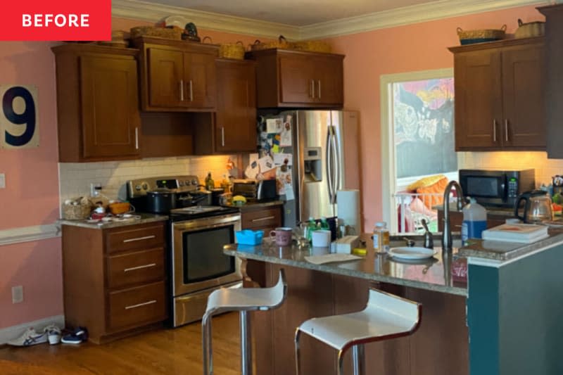 Kitchen with brown cupboards, stainless steel devices, pink walls and a crowded worktop with different objects.