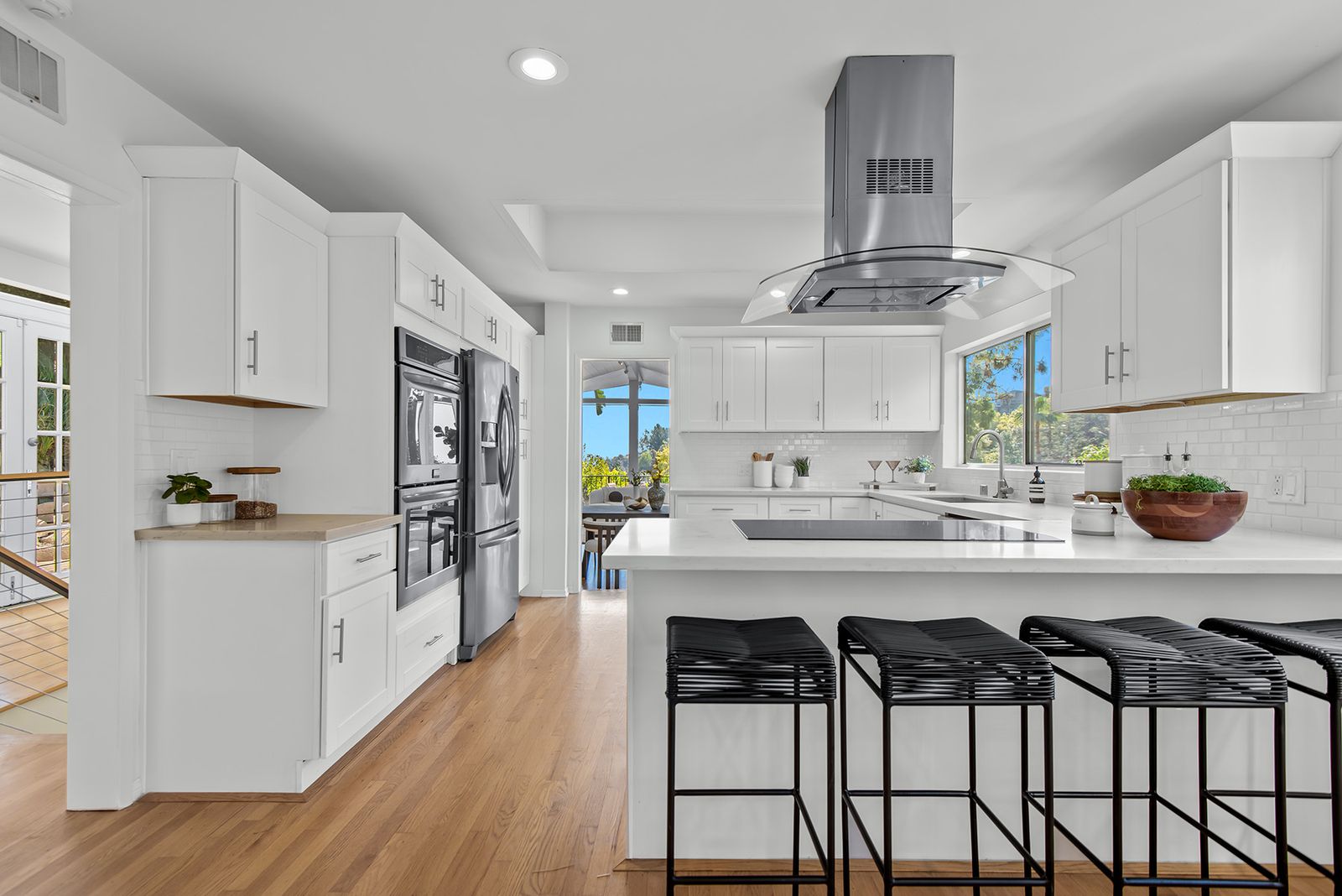 White kitchen with white upper and lower cupboards White kitchen Island Four black bar stool metal tank hood overhead