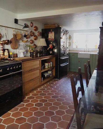 Rustic cuisine with hexagonal tile floor, wooden cabinets, black refrigerator and hanging copper cookware.