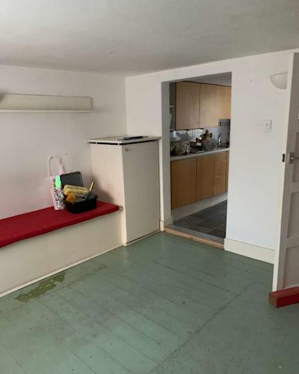 Small entrance with a red bench, a white fridge and a view of a kitchen with wooden cabinets.