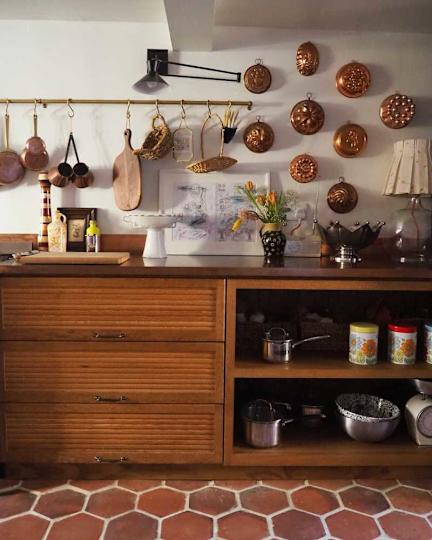 Wooden kitchen cabinet with three drawers, copper pots on the wall and a flower vase on the counter.