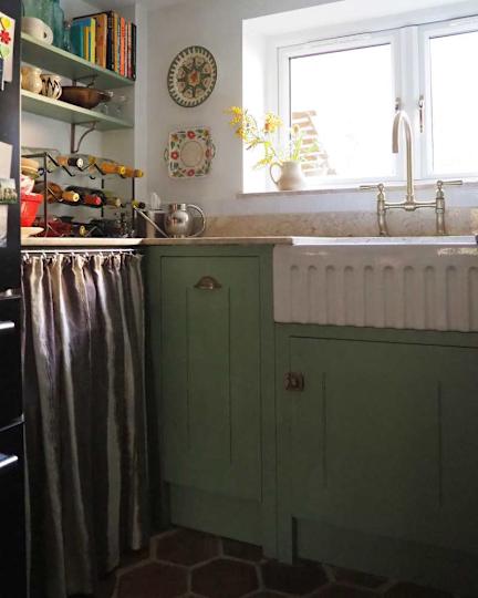 Cozy kitchen corner with a green closet, a sink, wine rack and decorative plates on the wall.