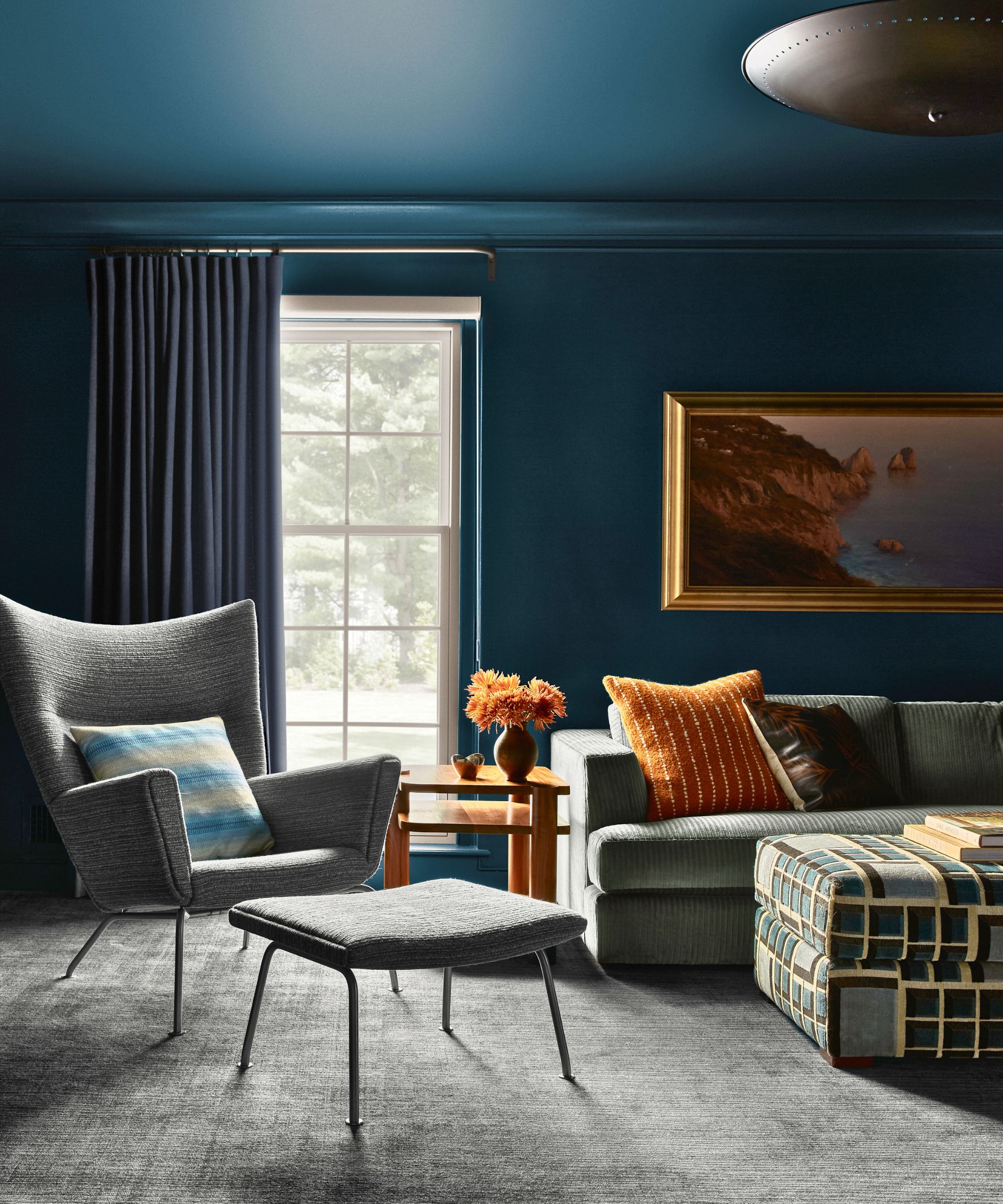 Living room color in dark blue soaked with gray sofa and armchair, orange throwing pillow and large paintings in a golden frame